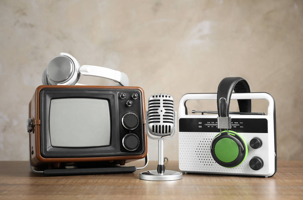Retro portable TV, radio, microphone and headphones on table against light wall - Valokuva, kuva