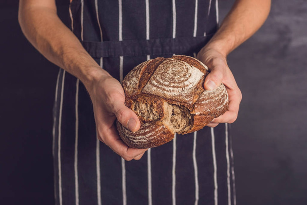 Baker man holding homemade rustic wheat bread in hands. Selective focus - Foto, Imagen