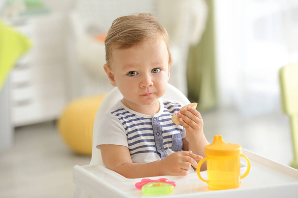 Adorable baby eating apple while sitting in highchair at home - Fotografie, Obrázek
