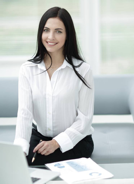 successful young woman sitting at a desk on a blurred background. - Φωτογραφία, εικόνα
