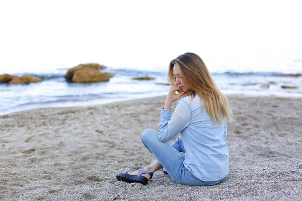lächelnde junge Frau ruht sich am Strand aus und posiert in der Kamera, sitzend - Foto, Bild