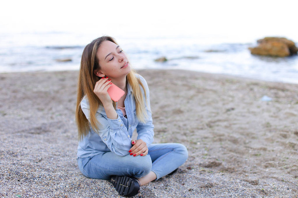 Ihana tyttö chattailee puhelimessa hymyillen ja istuu rannalla n
 - Valokuva, kuva