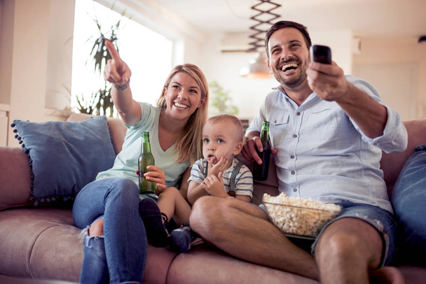Счастливая семья смотрит телевизор на диване дома. - Фото, изображение