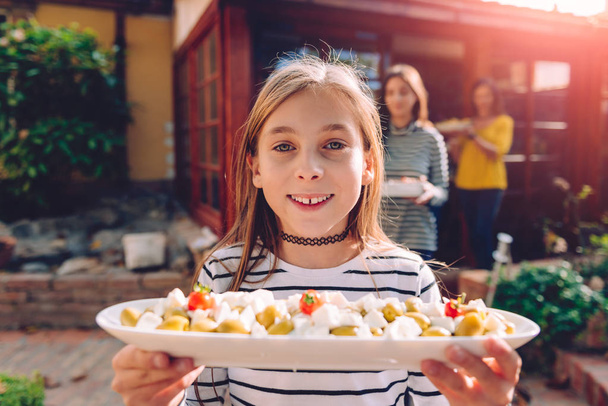 Happy girls carrying bowls with vegetarian salad at backyard patio - Foto, immagini
