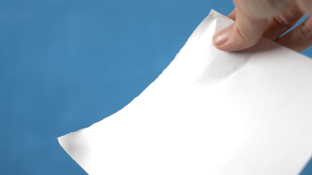 Handen scheuren van papier vel, close-up op een turkooizen achtergrond. 4k, slow-motion - Video