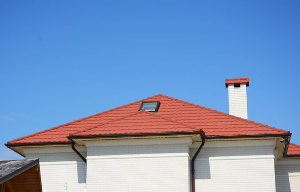 Fermer sur la fenêtre de lucarne grenier de la maison avec toit métallique rouge, gouttière, cheminée et caméras de sécurité
. - Photo, image