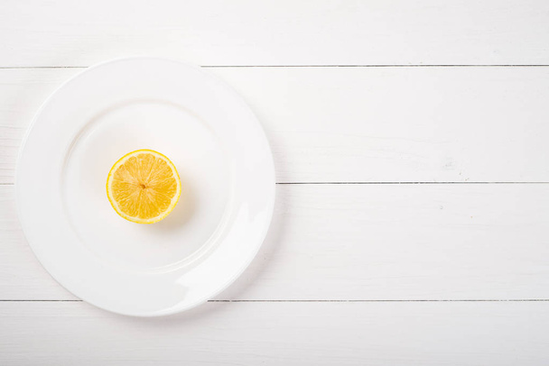Fresh lemon in a plate on wooden background. Half of lemon - Zdjęcie, obraz