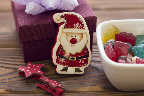 A toy santa, a bowl of candies and a gift box - Zdjęcie, obraz