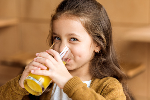 adorable kid drinking orange juice in cafe and looking at camera - Фото, изображение