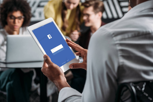 homem usando tablet com aplicativo facebook na tela com seus parceiros de negócios em segundo plano
 - Foto, Imagem