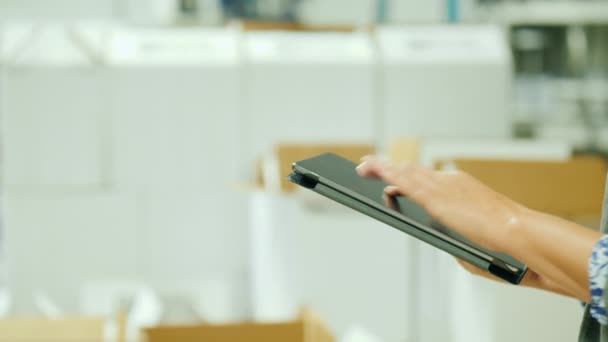 Logistics and stock accounting. Woman working with a tablet on the background of a stack of white boxes - Filmagem, Vídeo