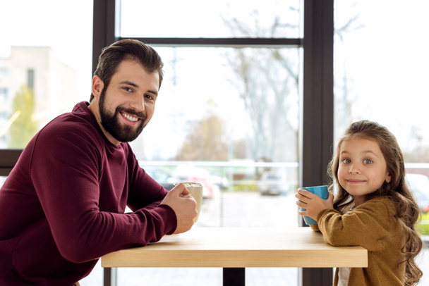 father and daughter holding cups and looking at camera - Photo, Image