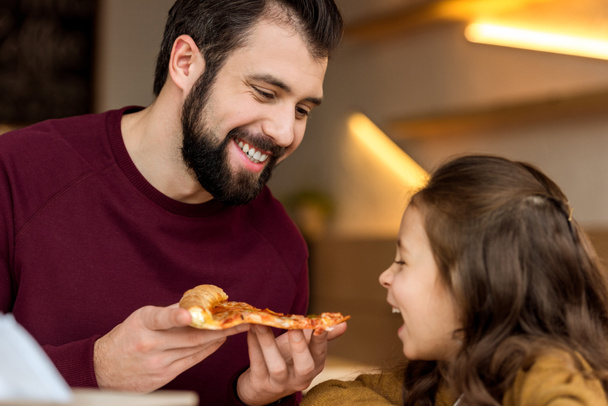 pai dando filha para morder um pedaço de pizza
 - Foto, Imagem