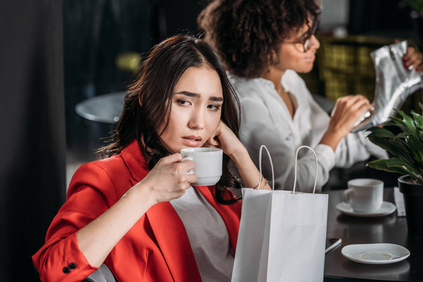 пригнічена молода жінка п'є каву після покупки
 - Фото, зображення