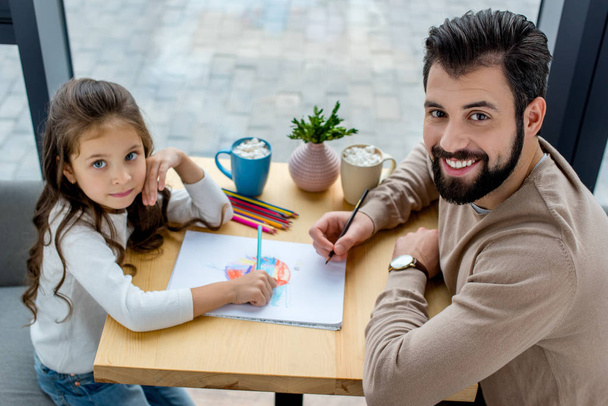 father and daughter drawing together and looking at camera - Photo, Image