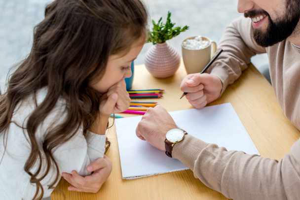 обрезанное изображение отца, держащего карандаш и показывающего часы дочери
 - Фото, изображение