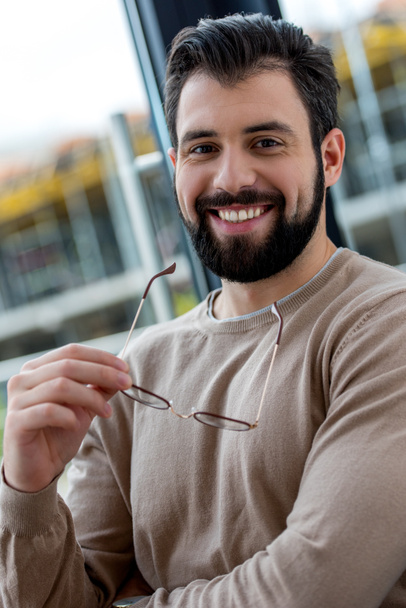 portrait of smiling handsome man holding glasses in hand and looking at camera - Foto, imagen