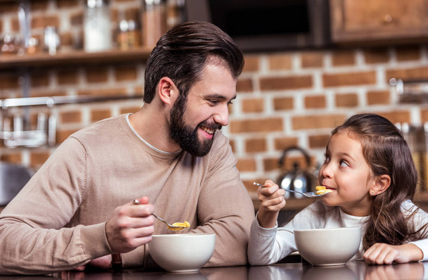 父と娘が朝食を食べるとお互いを見て笑みを浮かべてください。  - 写真・画像