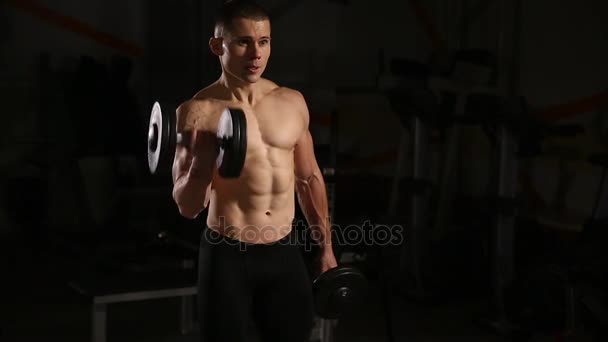 Sportos félmeztelen fiatal sport ember - fitness modell tart a súlyzó edzőteremben. Közeli kép: - Felvétel, videó