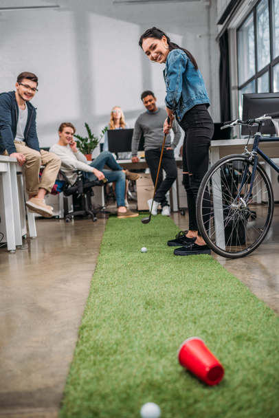 счастливая женщина играет в мини-гольф с коллегами в современном офисе
 - Фото, изображение