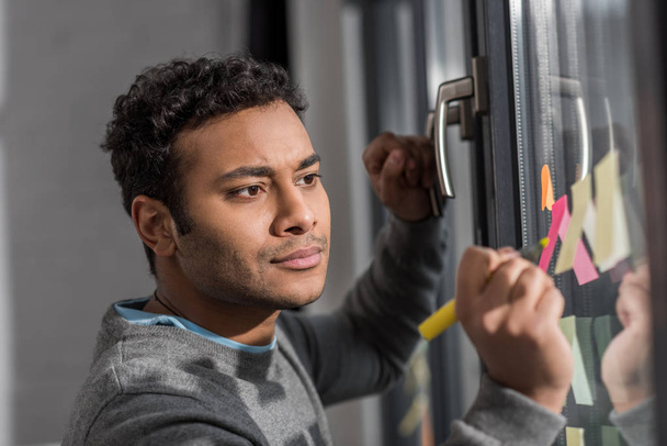 Junger Mann macht sich Notizen auf Aufkleber am Fenster - Foto, Bild