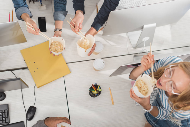 vista dall'alto delle mani ritagliate con cibo tailandese sul tavolo da lavoro in un ufficio moderno
 - Foto, immagini