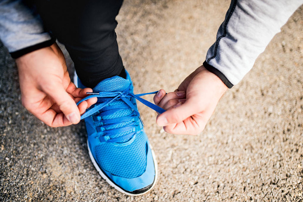 Unrecognizable young runner tying shoelaces. - Foto, afbeelding