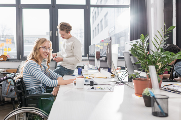 gelukkige rechtsonbekwame persoon in rolstoel werken bij moderne kantoor - Foto, afbeelding