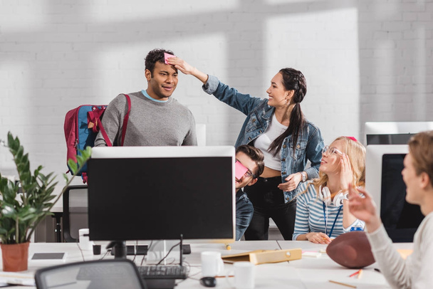 Frau klebt Aufkleber auf Kopf des Mannes im modernen Büro - Foto, Bild