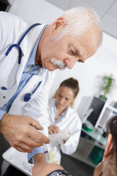 doctor injecting patient nurse in the background - Photo, image