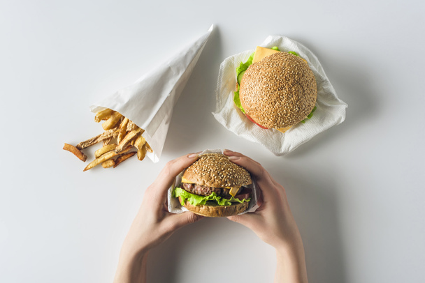 обрезанный вид рук с гамбургерами и картофелем фри в бумажном конусе, изолированный на белом
 - Фото, изображение