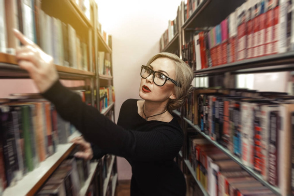 una giovane donna in biblioteca sceglie un libro
 - Foto, immagini