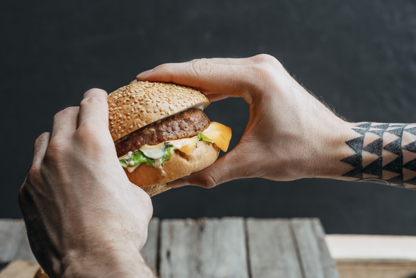 vista recortada del hombre sosteniendo sabrosa hamburguesa casera con queso
 - Foto, Imagen
