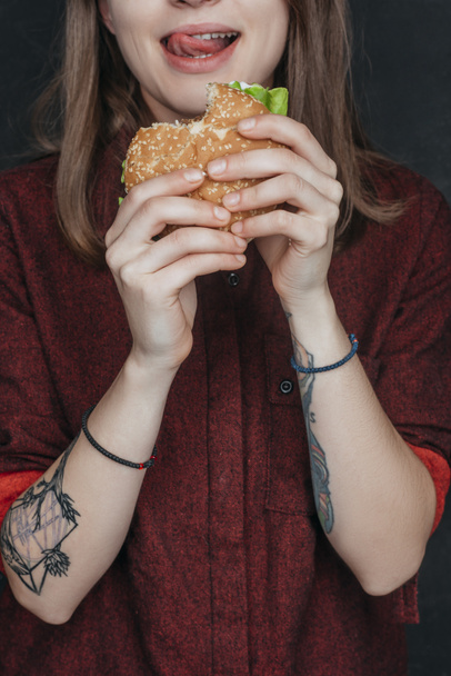cropped view of tattooed girl eating tasty hamburger - Photo, Image