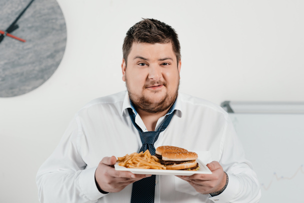 overweight businessman with hamburger and french fries in office - Photo, Image