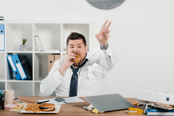overweight businessman eating hamburgers and french fries in office - Foto, Imagen