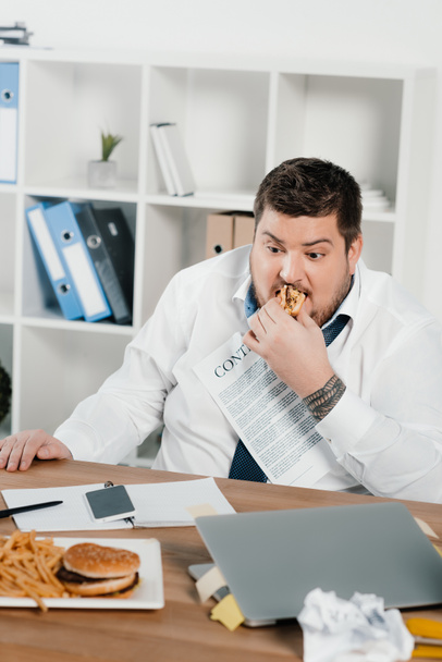 fat businessman eating hamburgers and french fries in office - Фото, изображение