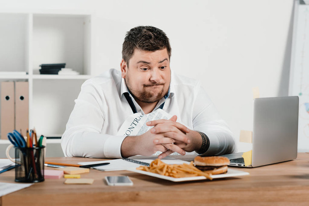 толстый бизнесмен обедает с гамбургером и картошкой фри в офисе
 - Фото, изображение