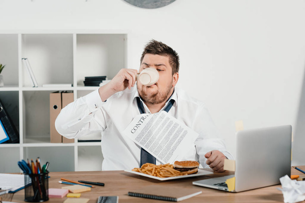gordo hombre de negocios comer comida rápida y beber café en la oficina
 - Foto, imagen