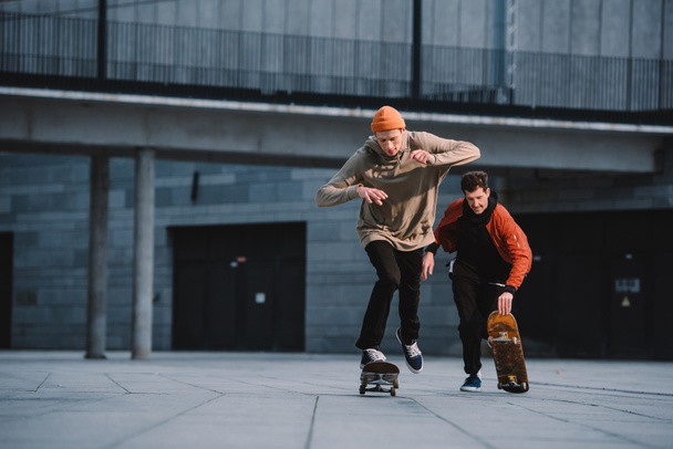 стильні молоді чоловіки в вуличному вбранні катаються на скейтбордах
 - Фото, зображення