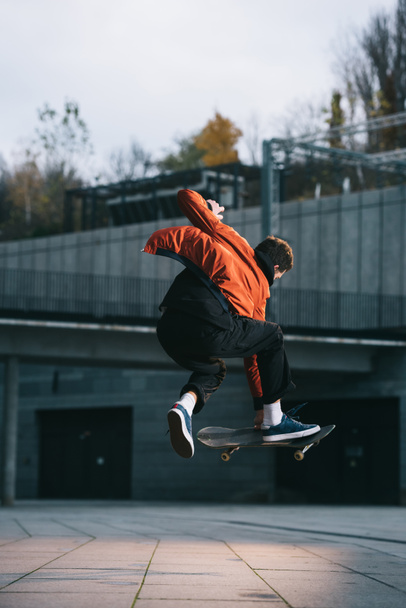 skateboarder en chaqueta roja realizando truco de salto en ubicación urbana
 - Foto, Imagen
