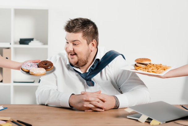 overweight businessman choosing donuts or hamburger with french fries for lunch - Photo, Image