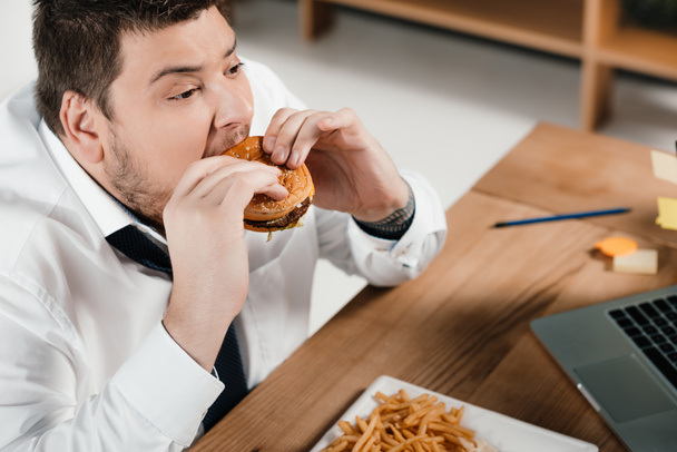 overweight businessman eating hamburger at workplace - Foto, Imagem