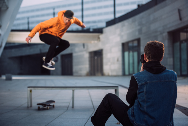 man taking photo of skateboarder jumping over bench - Photo, Image
