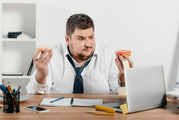 overweight businessman eating donuts at workplace - Φωτογραφία, εικόνα