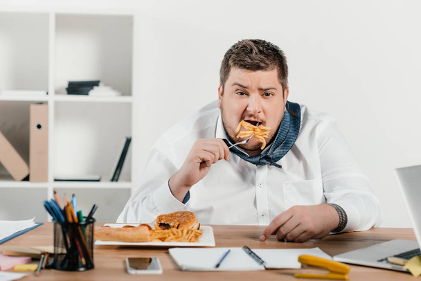 overweight businessman eating junk food at workplace - 写真・画像