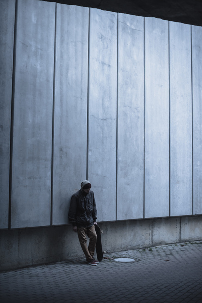 skateboarder with board leaning back on grey concrete wall - Fotografie, Obrázek