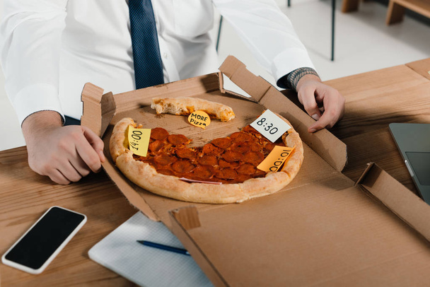 bijgesneden weergave van overgewicht zakenman pizza eten op werkplek  - Foto, afbeelding