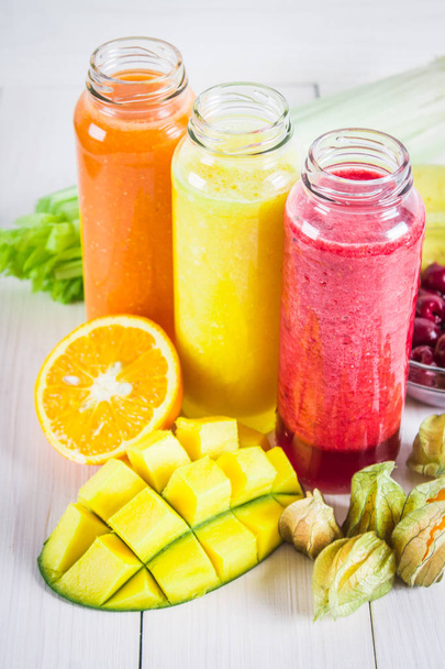 Multicolored smoothies in bottles of mango, orange, banana, celery, berries, on a wooden table. - Фото, изображение