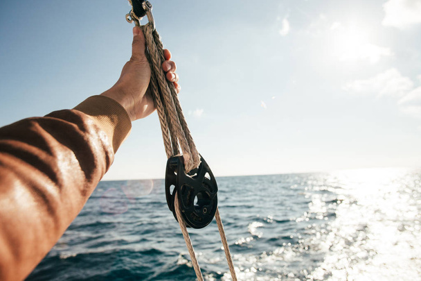 Professional sailor person hand holding rope on yacht boat during cruise in open sea - Foto, imagen
